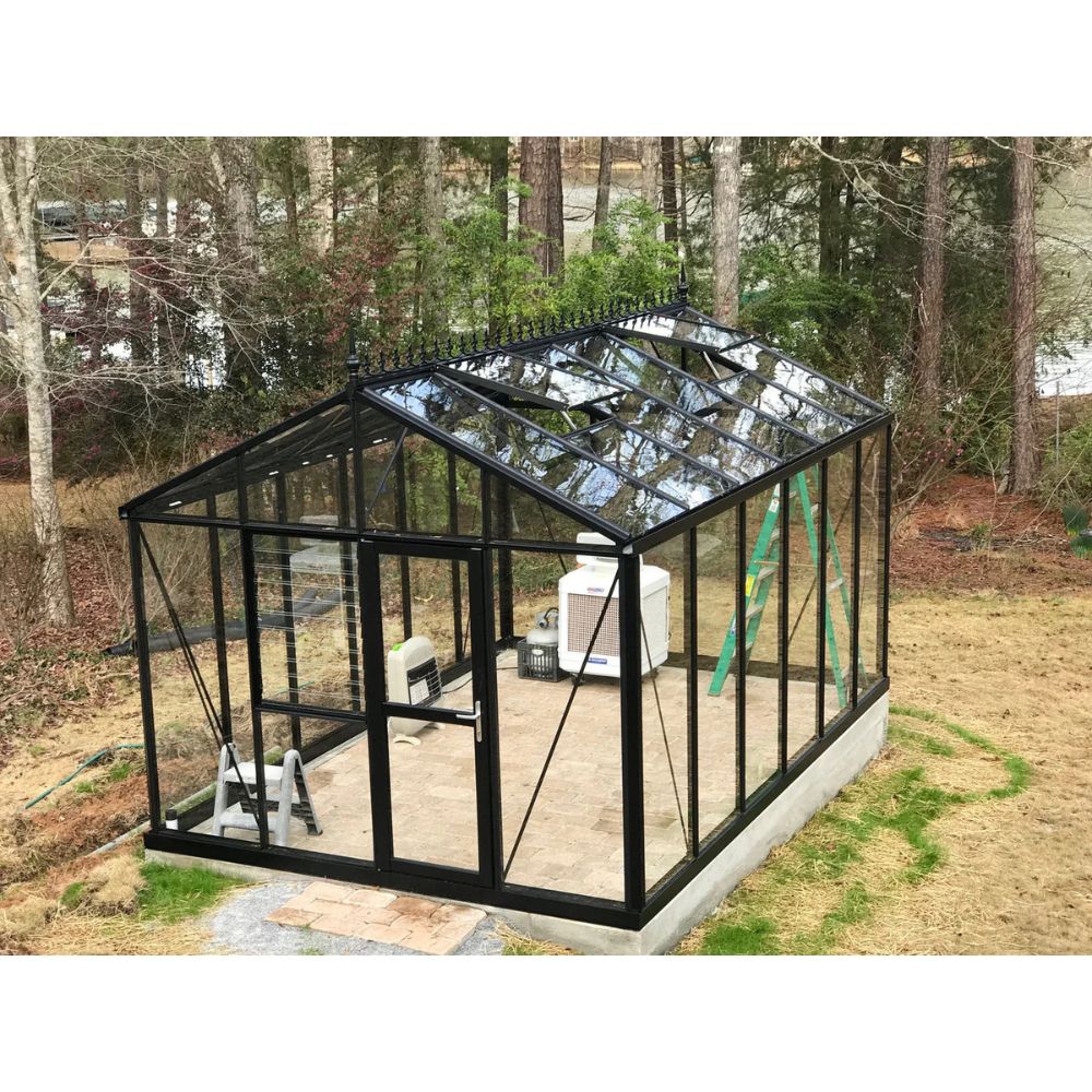 Black metal greenhouse with glass panels in a backyard setting