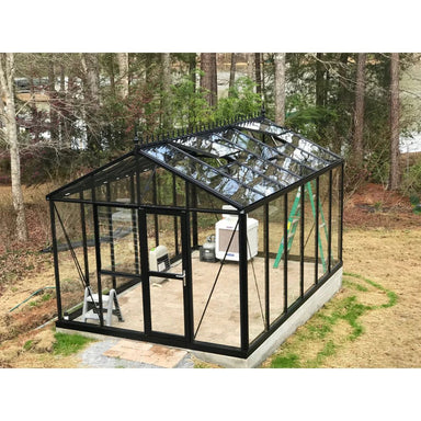 Black metal greenhouse with glass panels in a backyard setting