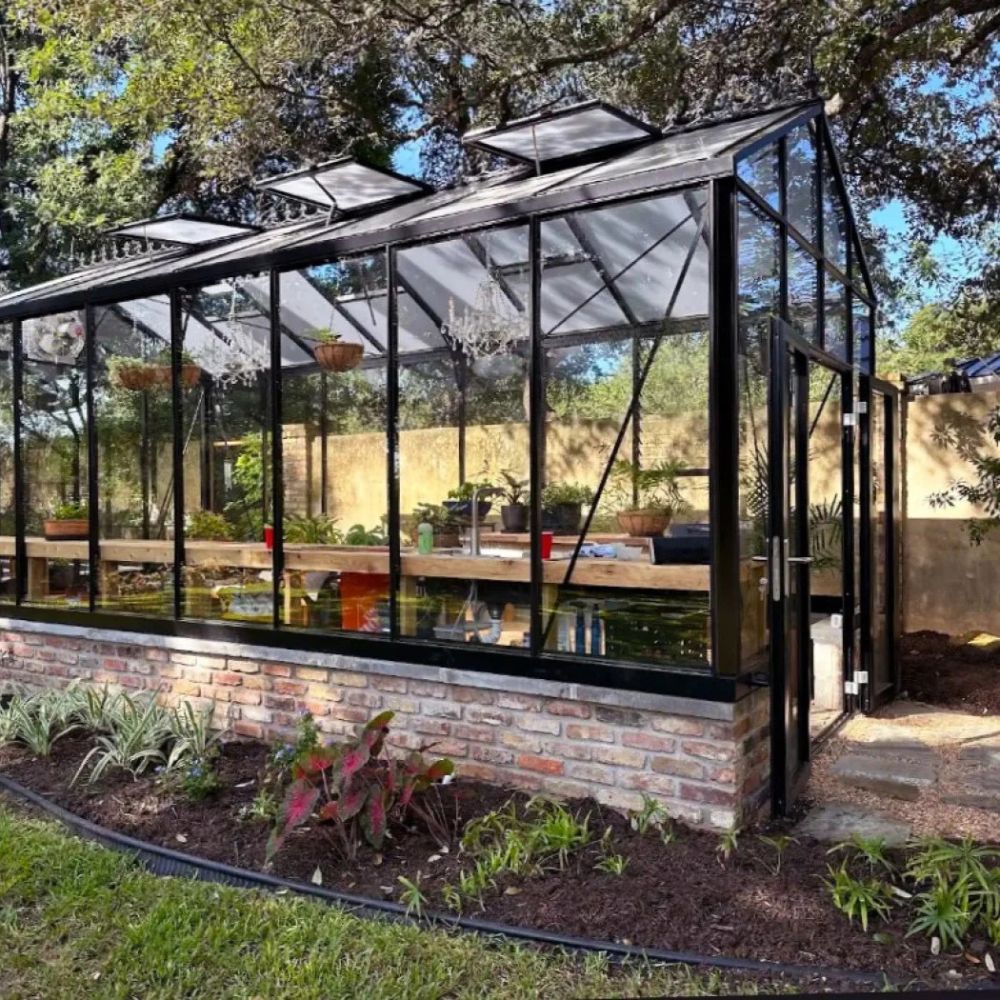 Large glass greenhouse with brick foundation and garden outside