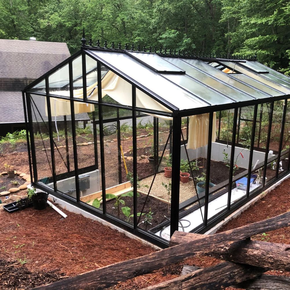 Glass greenhouse with black metal frame in a garden setting