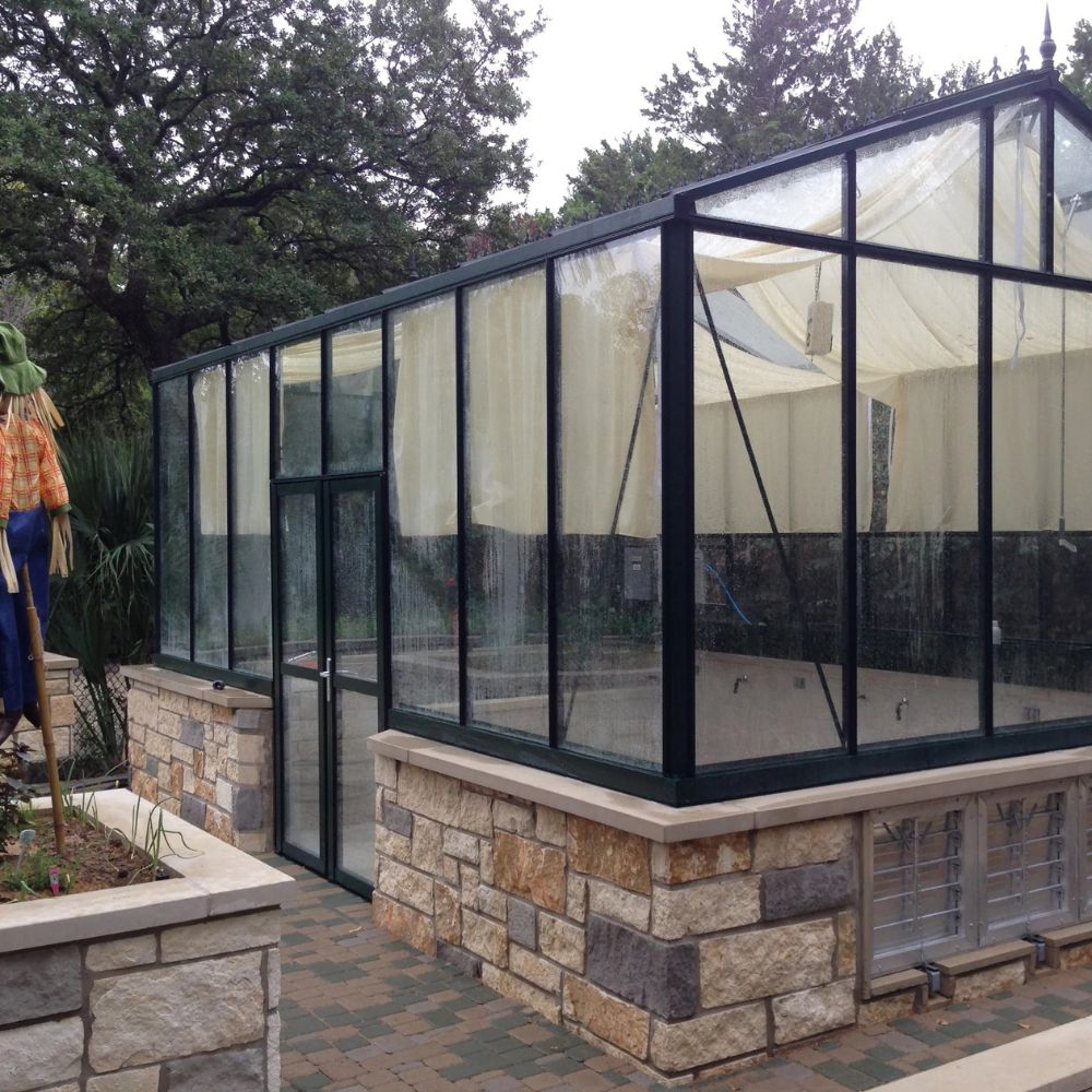 Glass greenhouse with stone foundation and surrounding trees