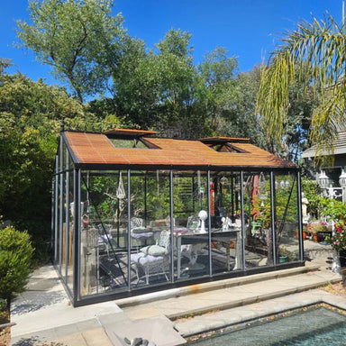 Glass greenhouse with wooden roof in a garden setting