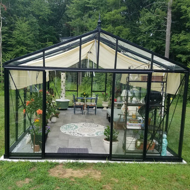 Greenhouse with glass walls and black frame, surrounded by greenery